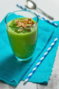 Grüner Smoothie im Glas auf türkisfarbenem Tuch mit zwei blau weiß geringelten Stohhalmen und Silberlöffel Grüner Smoothie im Glas auf türkisfarbenem Tuch mit zwei blau weiß geringelten Stohhalmen und Silberlöffel